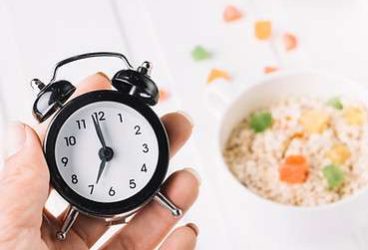 person-s-hand-holding-alarm-clock-hand-breakfast-table